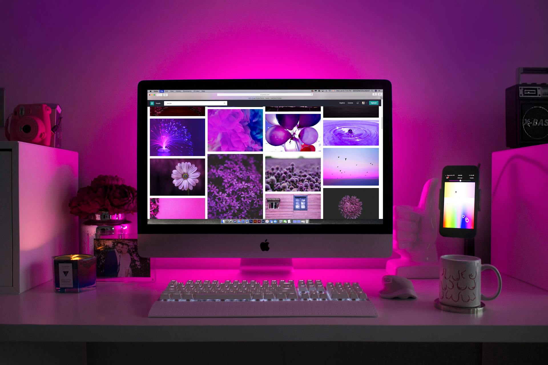 A desktop computer displaying purple-themed images, illuminated by purple lighting, with a keyboard and mug on the desk.