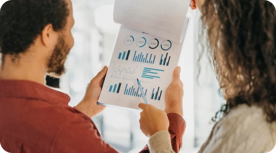 A man and a woman reviewing a data report filled with charts and graphs.