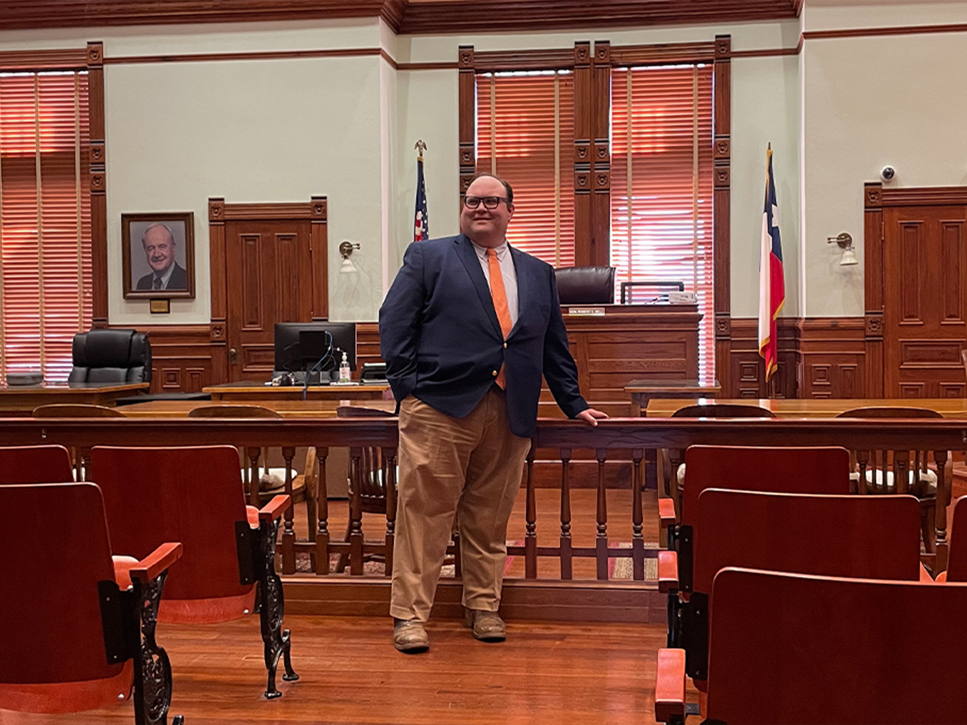 Brian M. Cromeens standing in a courtroom with wood paneling and an American flag.