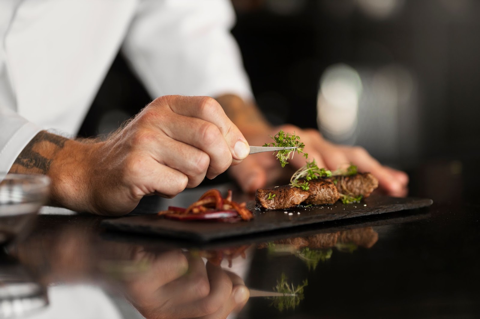 Chef delicately garnishing a plated dish with fresh herbs in a fine dining setting.