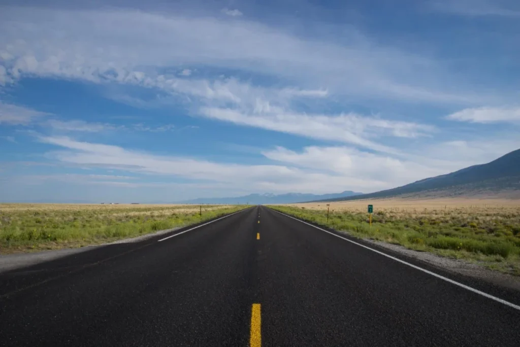 A long, open road stretching into the distance with clear skies and mountains in the background.